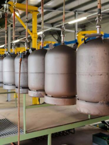 Sandgestrahlte, noch unbeschichtete Gasflaschen hängen zur Weiterbearbeitung an der Anlage