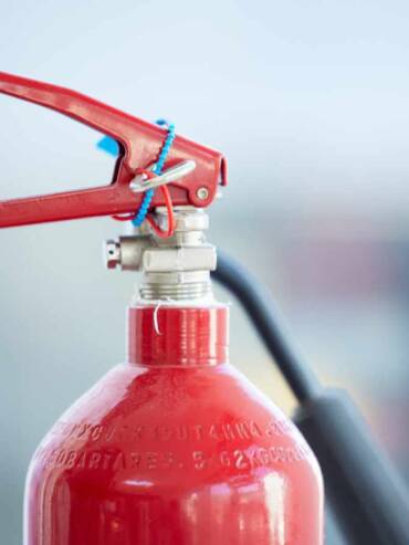 Nahaufnahme eines roten Feuerlöschers mit Auslösehebel, Sicherungsstift und Schlauch.